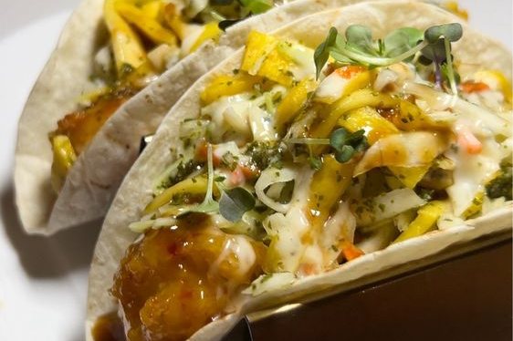 Two jerk-glazed fish tacos with mango slaw on a plate at Sugar'd